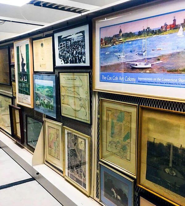 Framed artwork, maps and archival prints stored on mobile shelving screens in a museum collections room