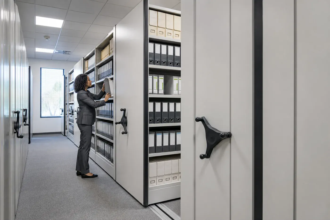 Employee retrieving a binder from electric high-density mobile shelving in an office records room