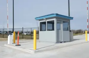 Prefabricated guard booth at a vehicle checkpoint with gate arms and yellow bollards