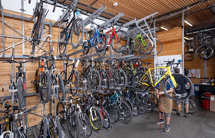 Rows of bicycles stored vertically on a Vidir Bicycle Merchandising System in a bike shop service area