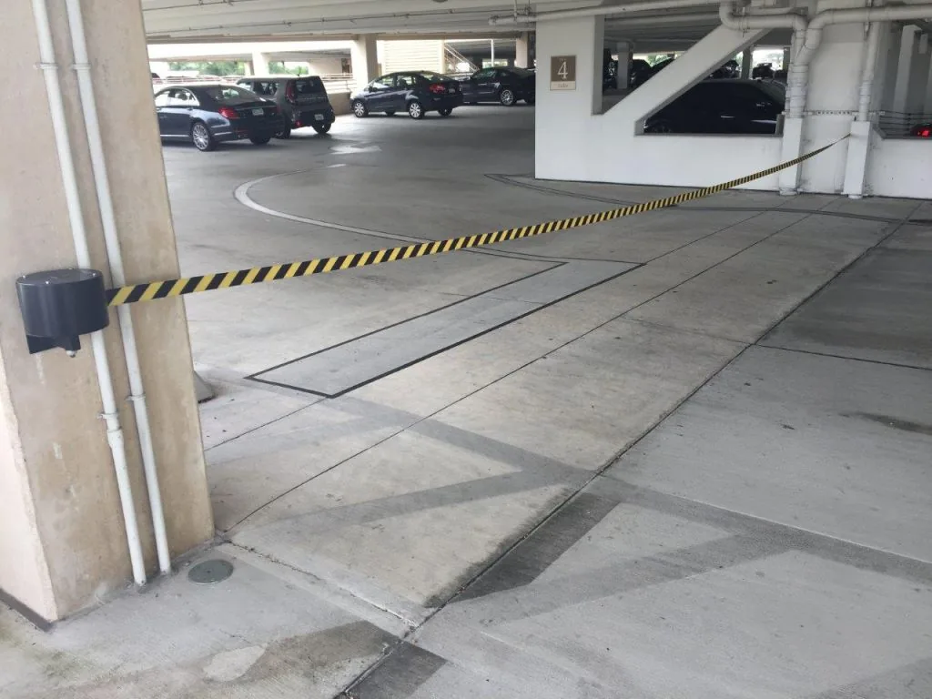 Long-span wall-mounted retractable belt barrier closing a parking garage lane with a black and yellow belt
