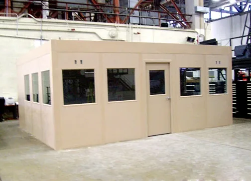 Beige prefabricated modular office room with windows and a door installed inside an industrial plant