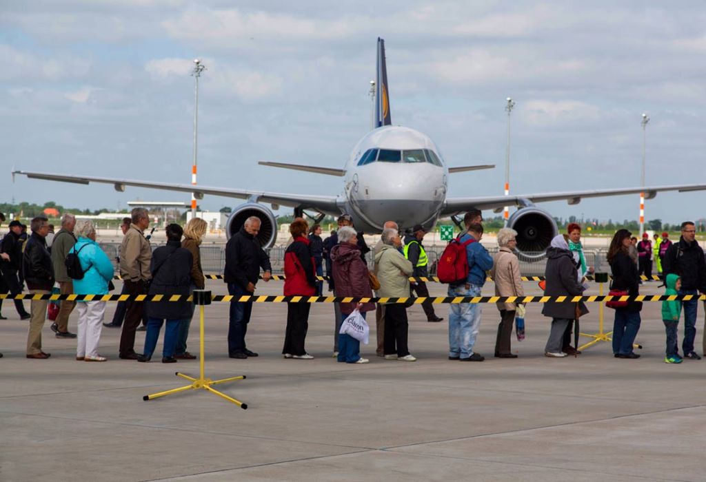 Passengers walking to a regional aircraft on the tarmac beside a long yellow and black retractable belt on a stand mount