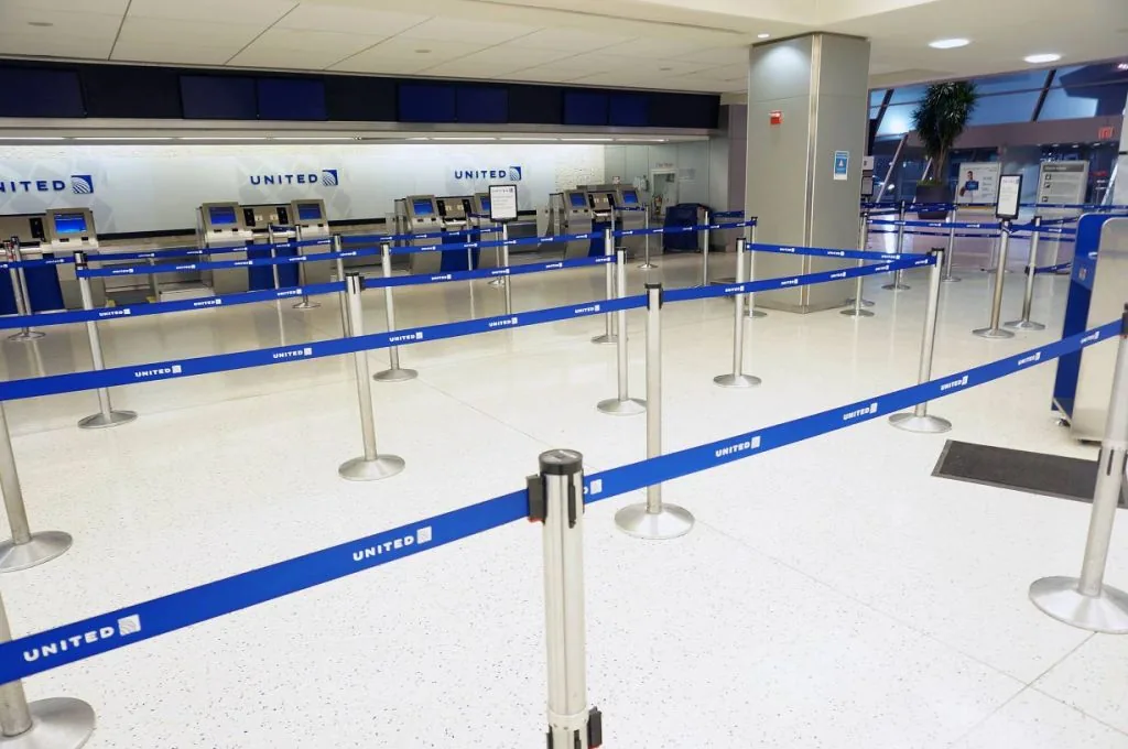 Airline check-in hall with polished stanchions and blue branded retractable belts forming switchback lanes