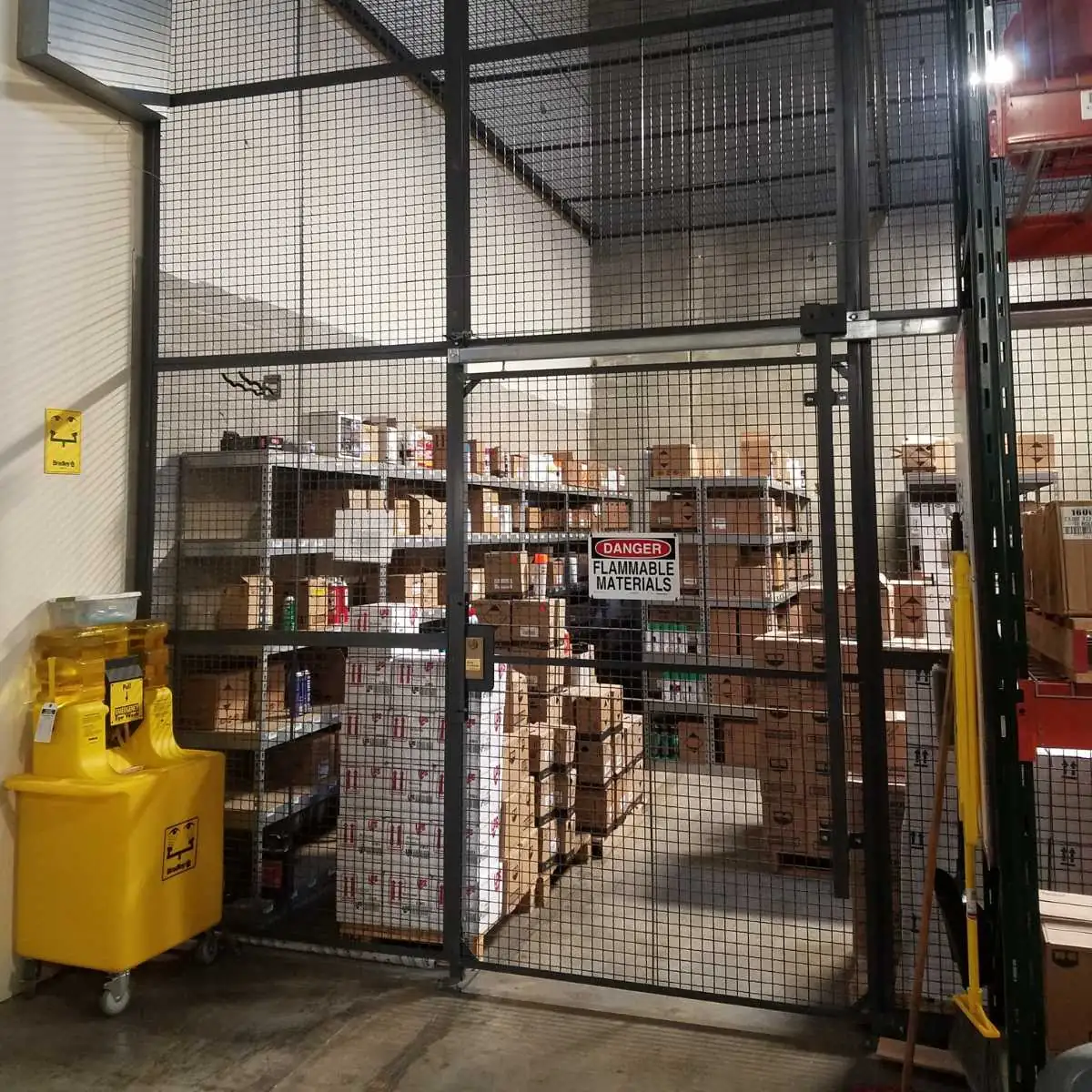 Floor-to-ceiling wire mesh aerosol storage cage with a self-closing door around shelving of aerosol products