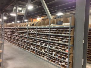 Long run of steel parts room shelving with cardboard bin boxes holding small boxed auto parts