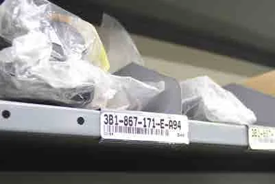 Part-number label on the edge of a Borroughs Flexi-Bin shelf below bagged parts