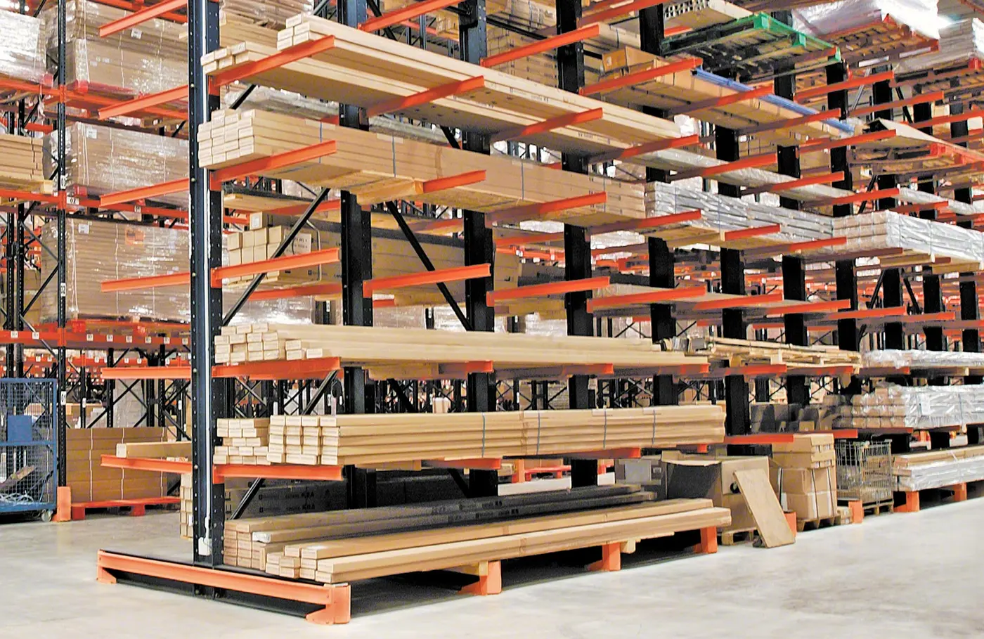 Indoor cantilever rack with lumber bundles on orange arms and orange protectors at the base ends facing the aisle
