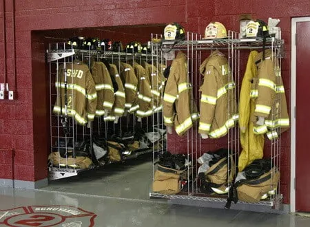 Wall mounted chrome Ready Rack turnout gear storage with helmets on the top shelf in a fire station