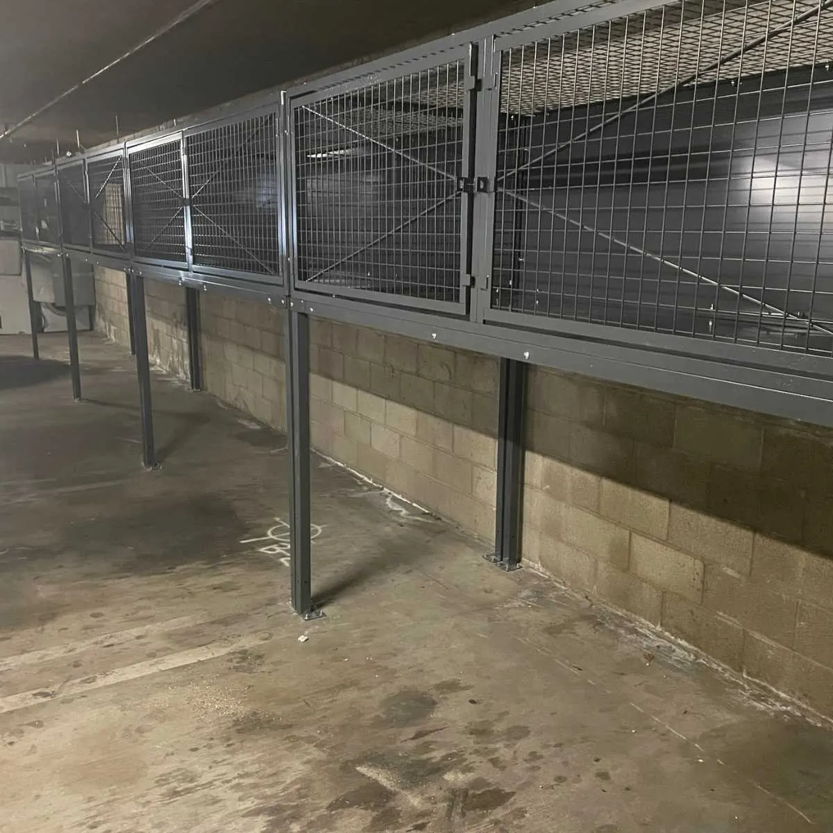 Wall-mounted wire mesh storage lockers above parking spaces in a condominium garage