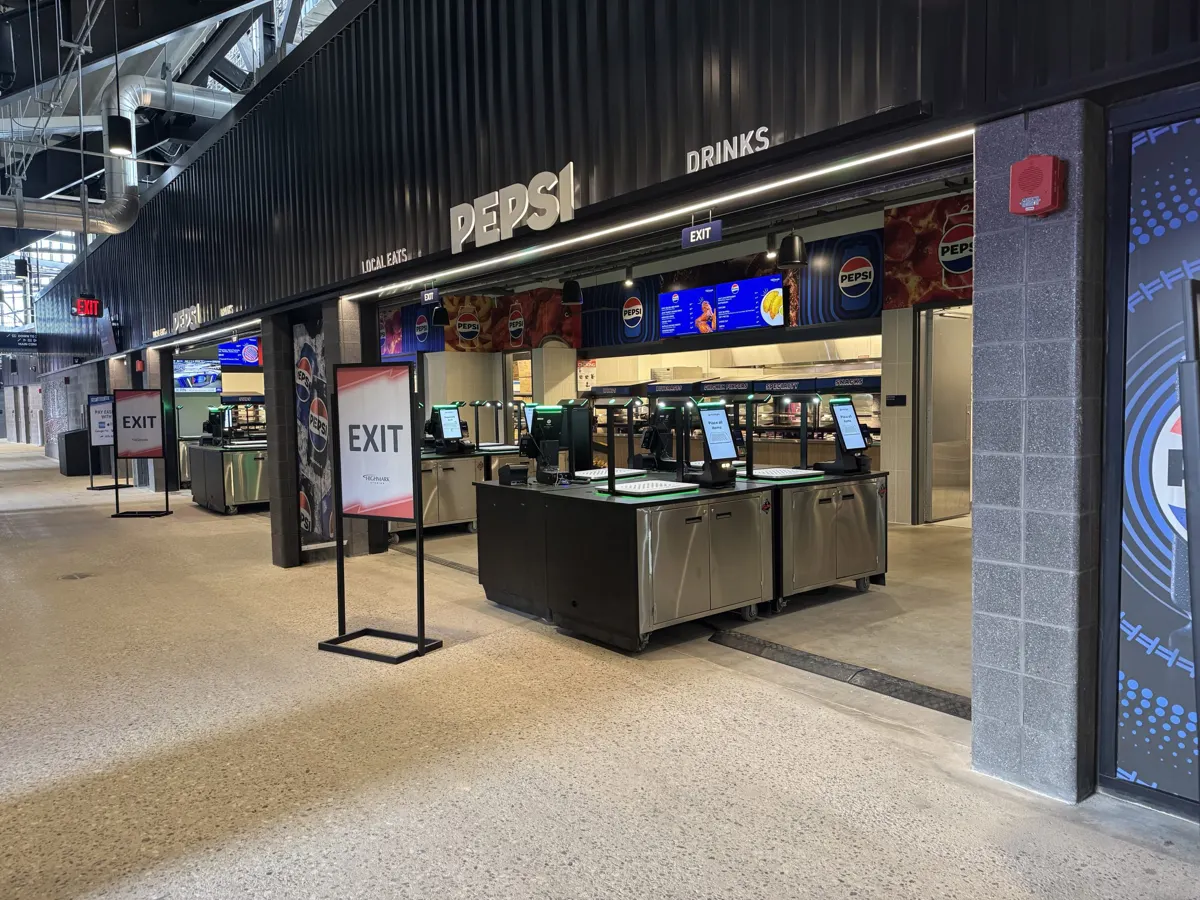 Floor-standing EXIT sign frames along a stadium concourse beside concession stands