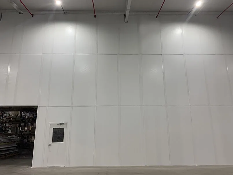 Full-height white modular partition wall closing off a warehouse area, with a personnel door and an open doorway into the racking area beyond