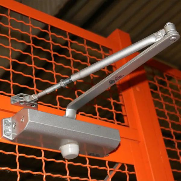 Hydraulic door closer mounted on an orange wire mesh cage door so it closes and latches on release