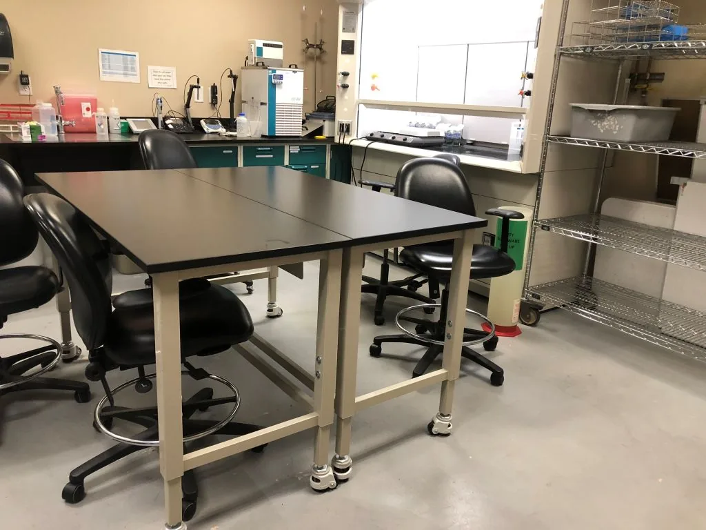 Laboratory tables with black resin tops on steel frames with lab chairs in a clean lab