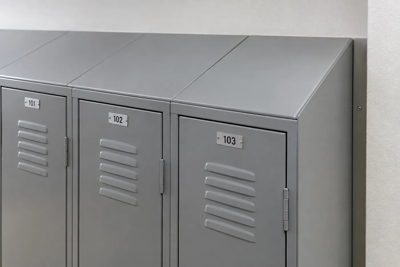 Close-up of gray steel lockers with angled sloped tops running back to the wall and aluminum number plates on each door