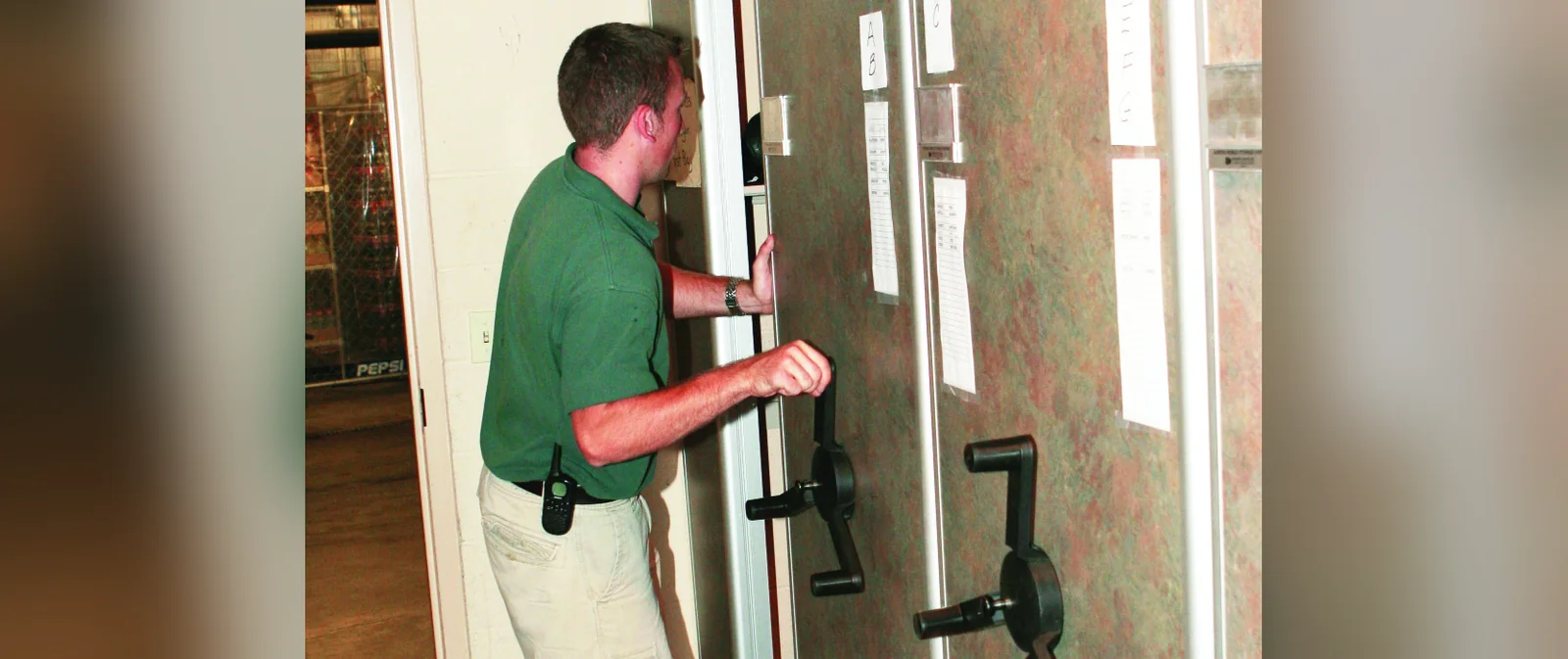 Staff member turning the handwheel on mechanical-assist mobile shelving to open an aisle in an athletic storage room