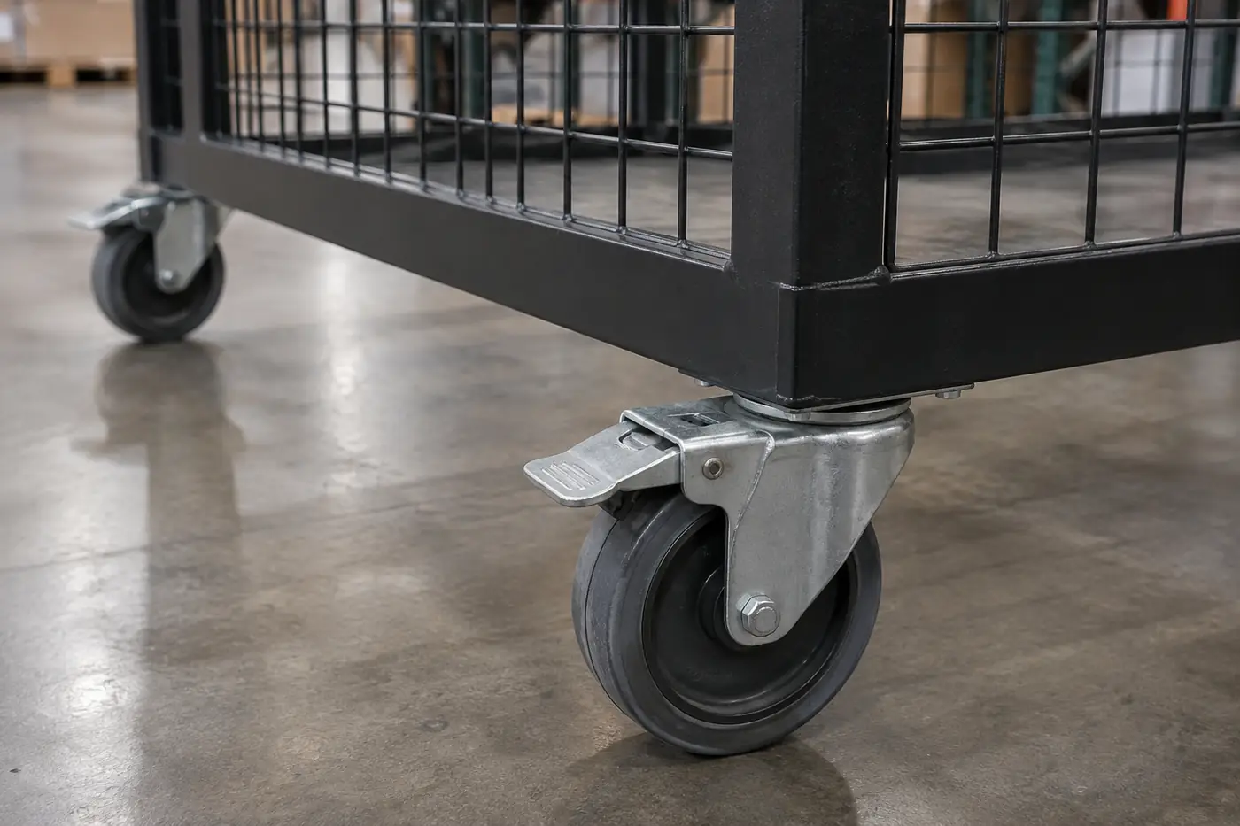 Close-up of a polyurethane swivel caster with the foot brake engaged under a black wire mesh mobile security cage on a concrete floor