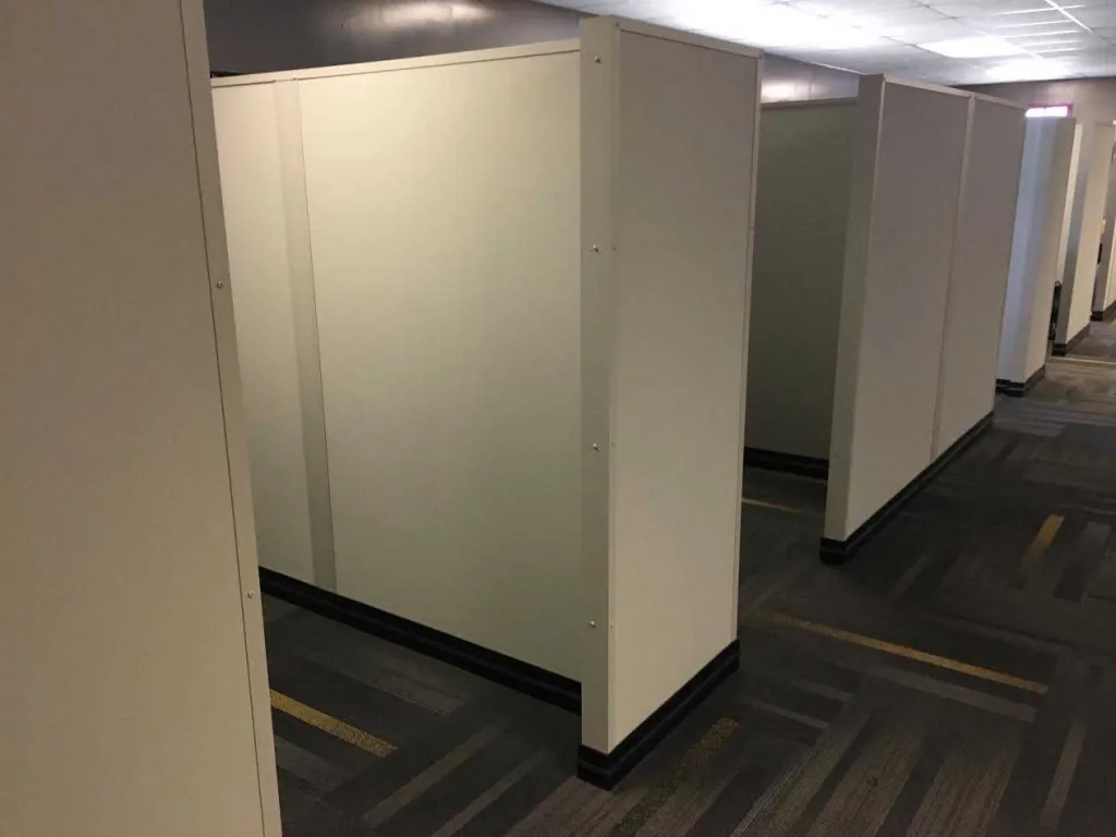 Modular panel walls about door height forming separate work cubicles along a carpeted corridor