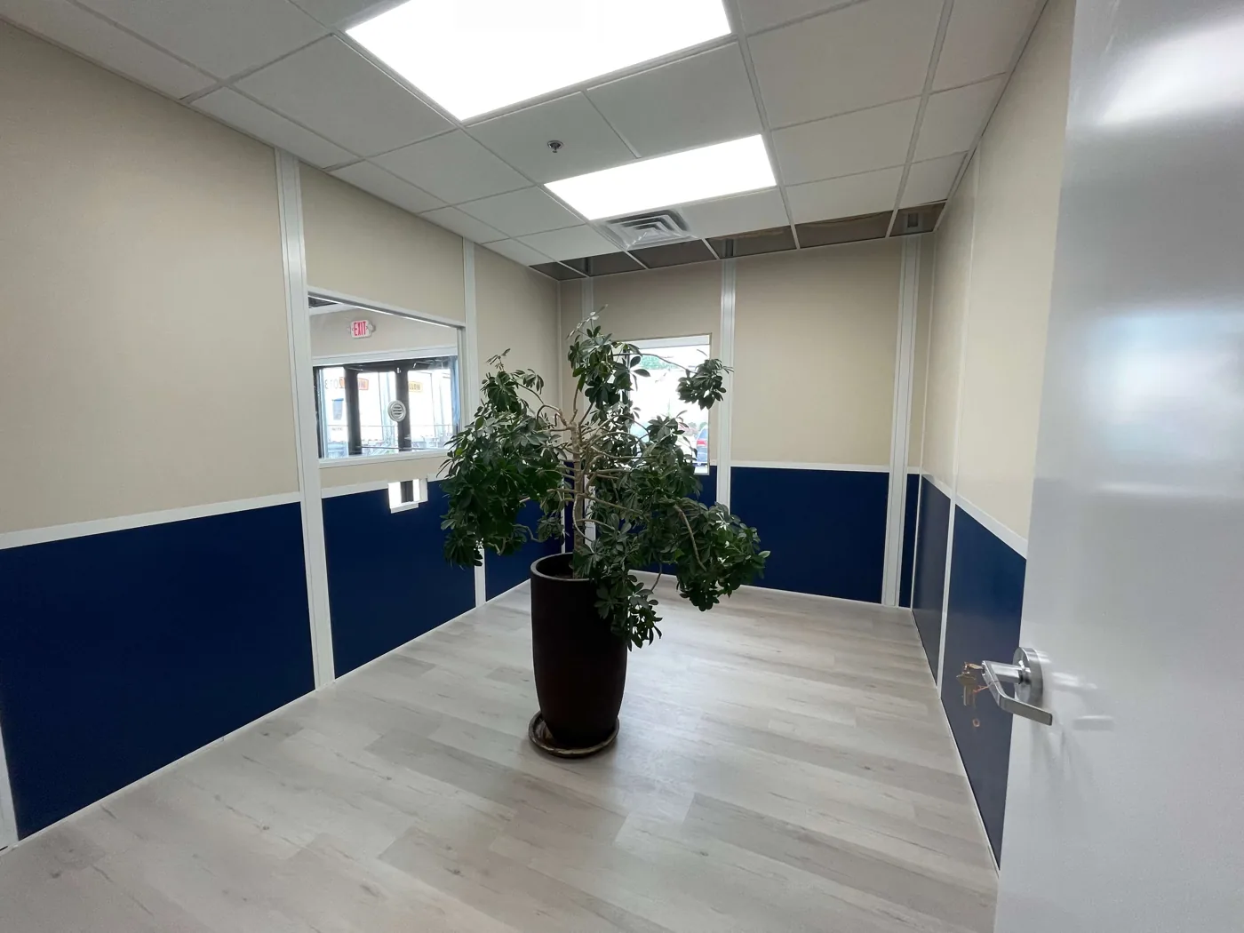 Room built from modular wall panels with blue lower panels, beige upper panels, an interior window and a drop ceiling