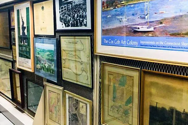 Framed paintings, prints and historic maps hung on wire mesh art storage screens in a museum collections room