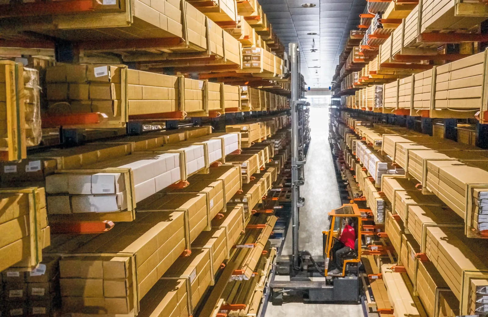 Operator on a narrow-aisle side-loading truck working between cantilever racks stocked with long boxed product