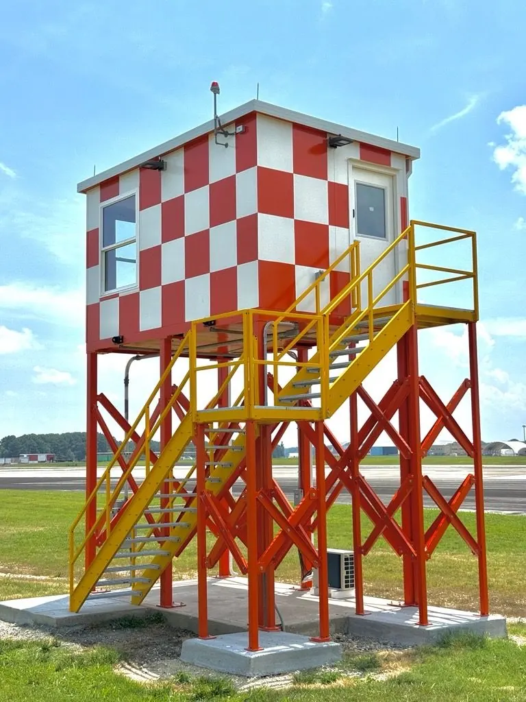 Red and white checkered elevated observation cab on a steel frame with a stair at an airfield