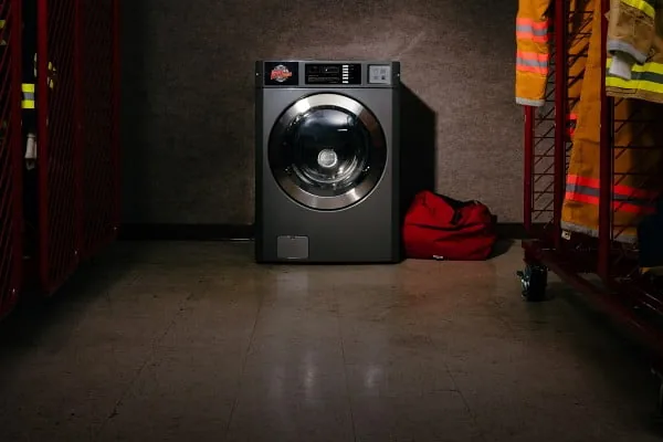 Front-load PPE extractor washer in a decon room beside turnout gear racks