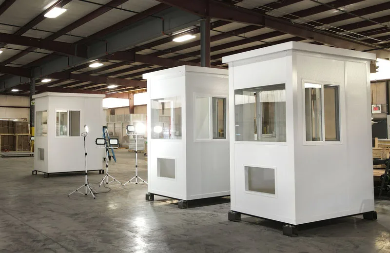 Three finished white prefabricated booths with sliding windows standing on a factory floor before shipping