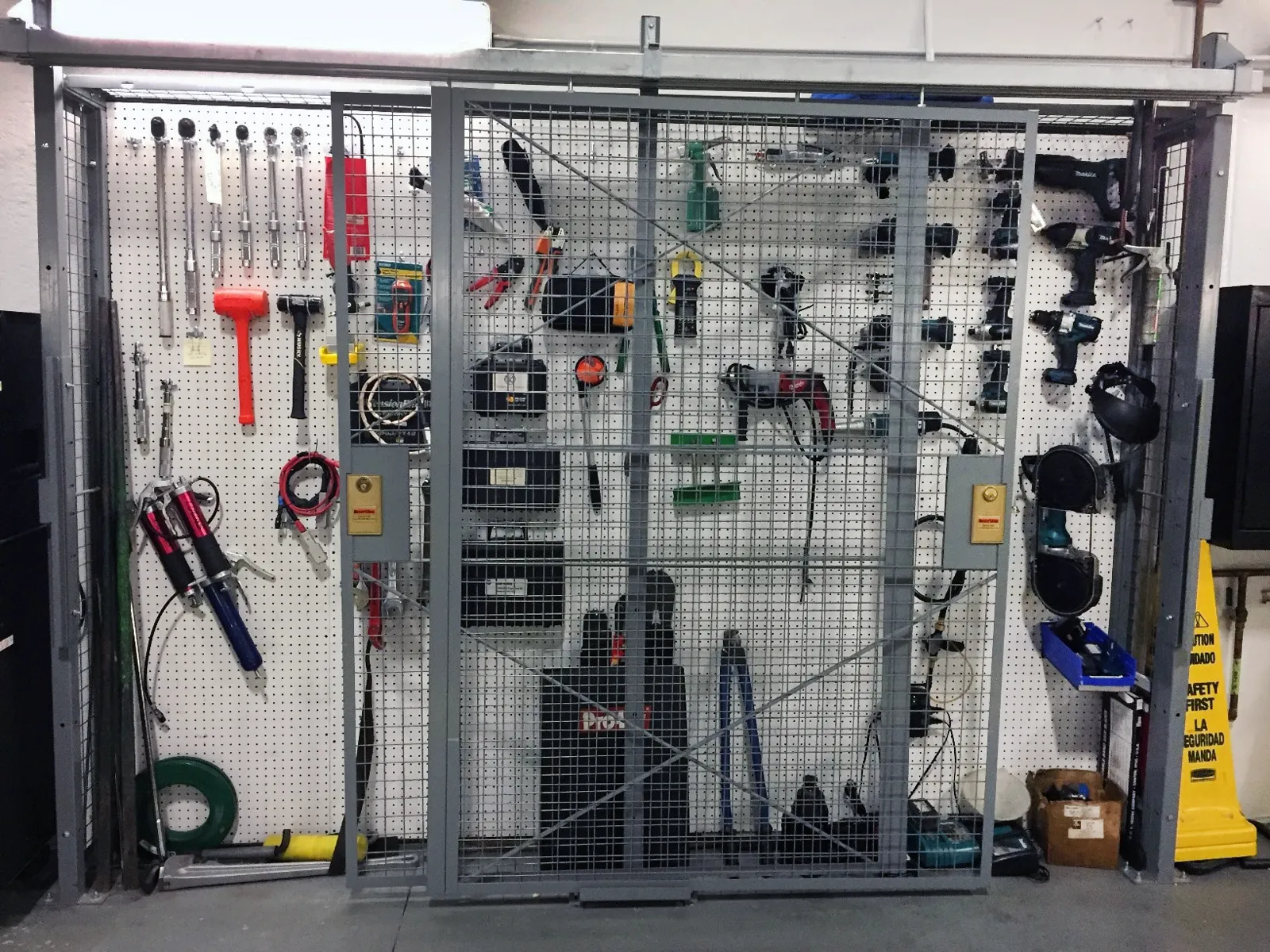 Gray SpaceGuard BeastWire welded wire tool crib with a sliding door in front of a pegboard tool wall
