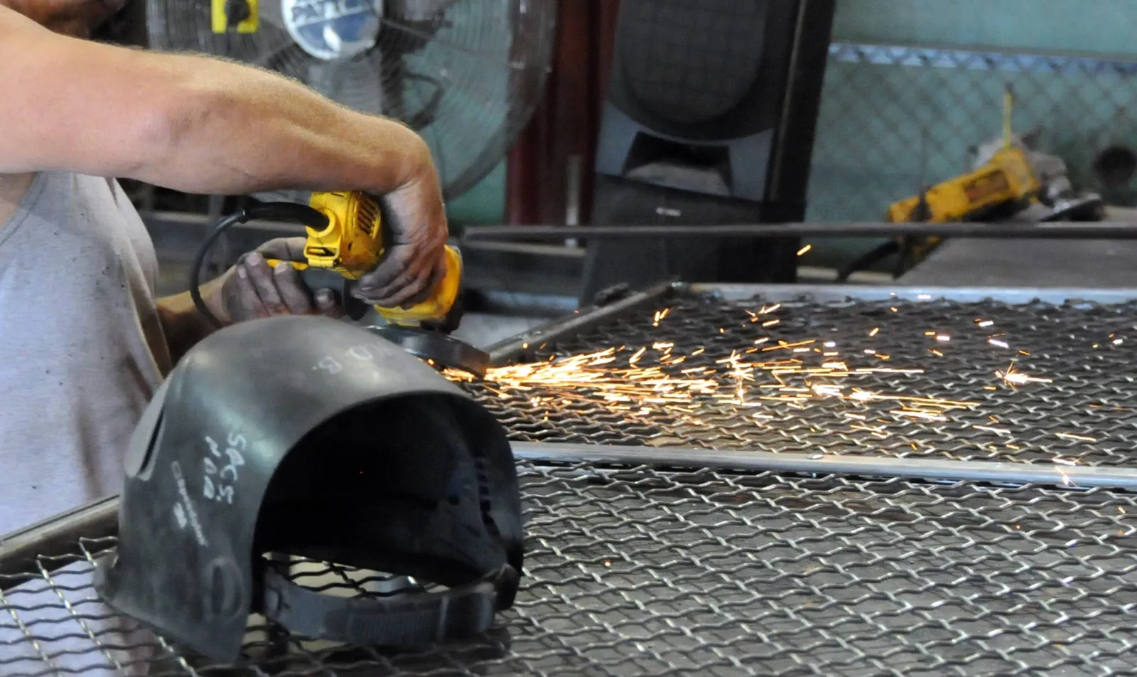 Worker grinding a FordLogan woven wire panel frame at the SpaceGuard factory