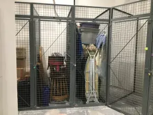 Gray welded wire mesh tenant storage cages with numbered padlocked doors holding tenant belongings