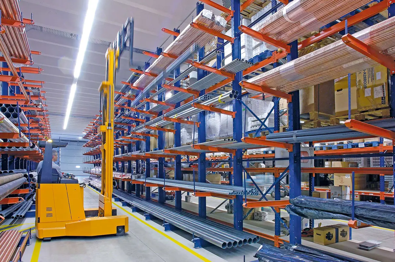 Tall indoor cantilever rack row with tube and pipe bundles running along the arms and a walkie stacker in the aisle