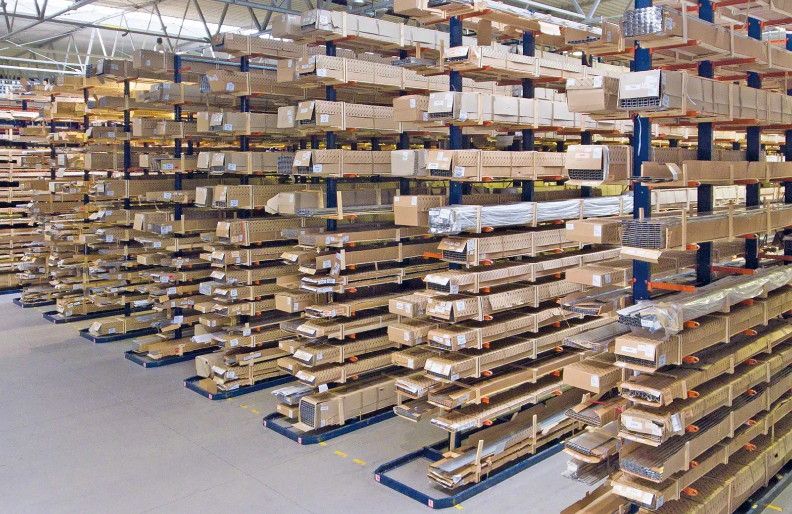 Rows of tall cantilever racks holding wood boards, panels and long cartons on many arm levels