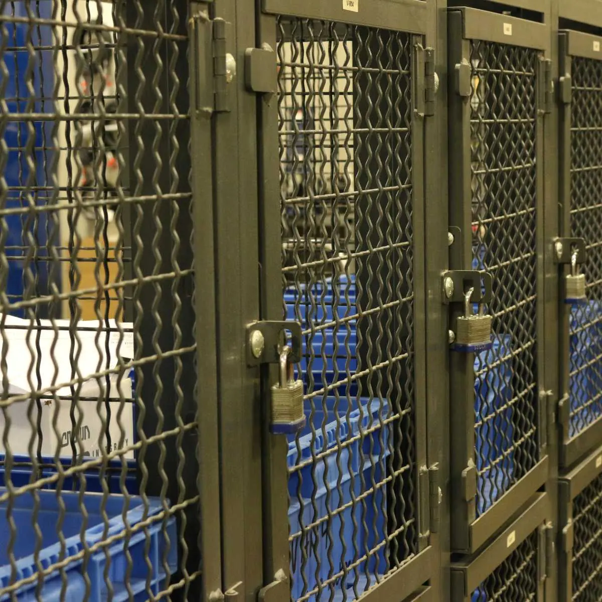 Padlocked wire mesh technician locker doors with parts bins visible inside