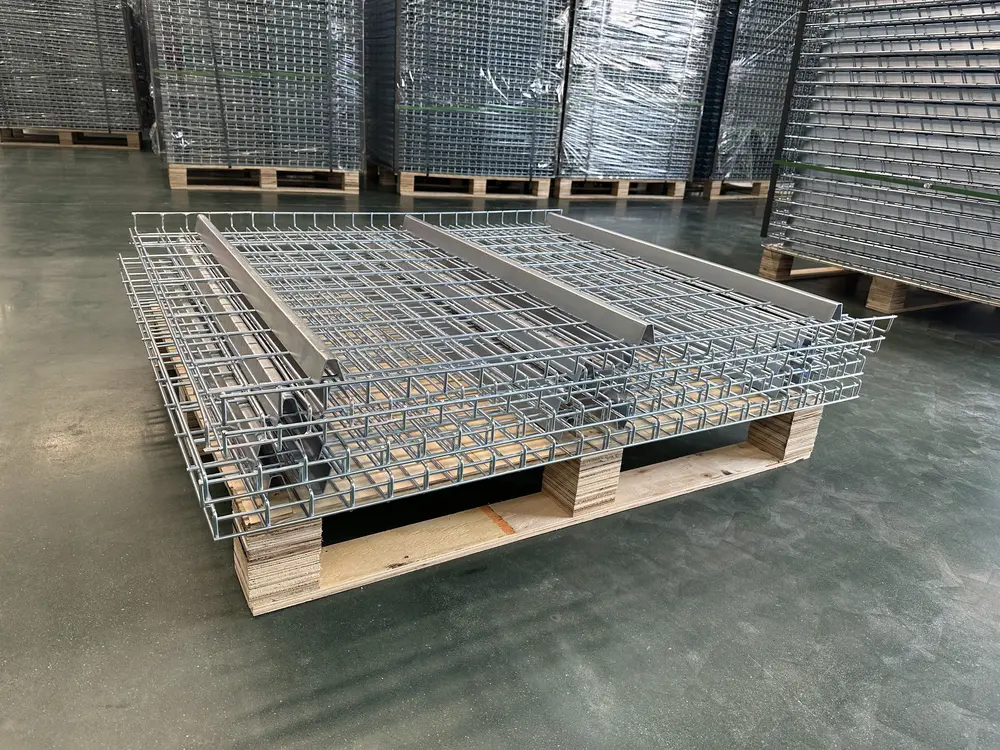 Unpainted wire mesh pallet rack decks with formed steel support channels, stacked on a wooden pallet in a warehouse