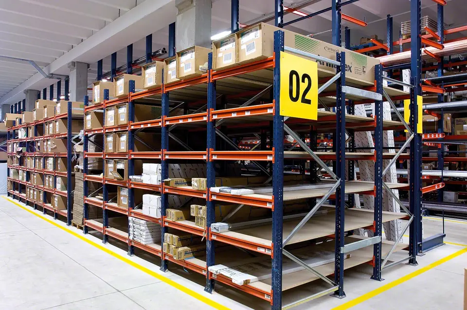 Wide span shelving bays with particleboard decks holding cartons, with a yellow aisle marker sign in a distribution center