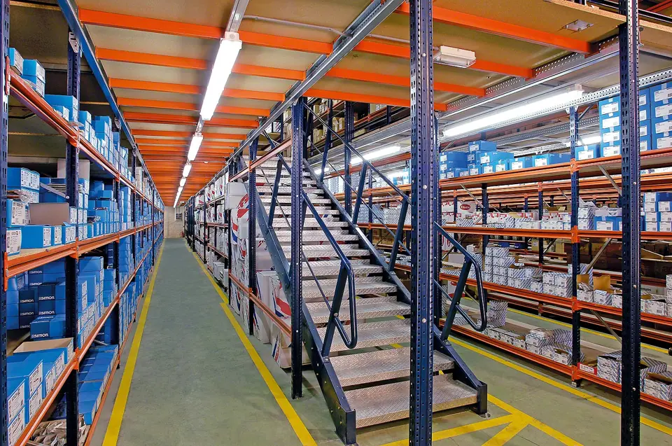 Two-level wide span shelving system with an elevated walkway and steel stairs between aisles of boxed parts