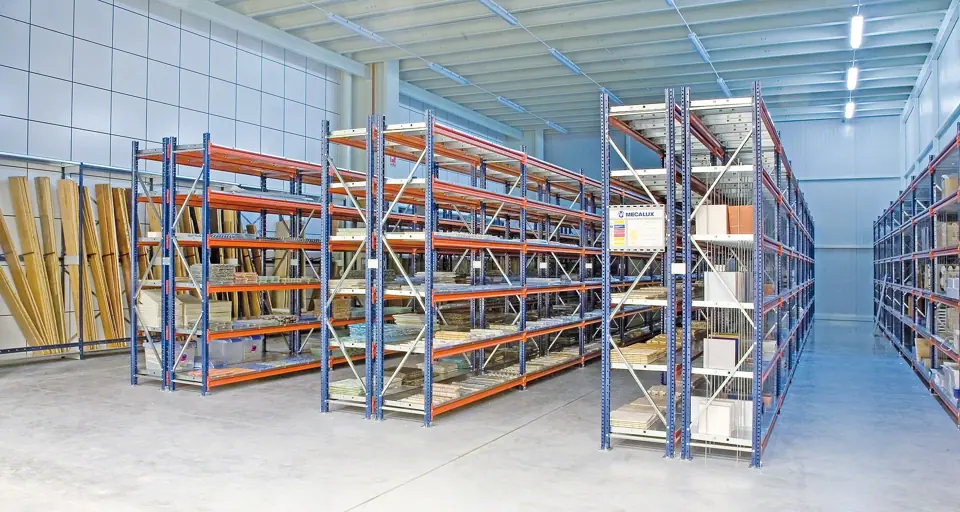 Freestanding runs of wide span shelving about 8 feet tall with blue frames, orange beams and boxed stock on every level in a warehouse