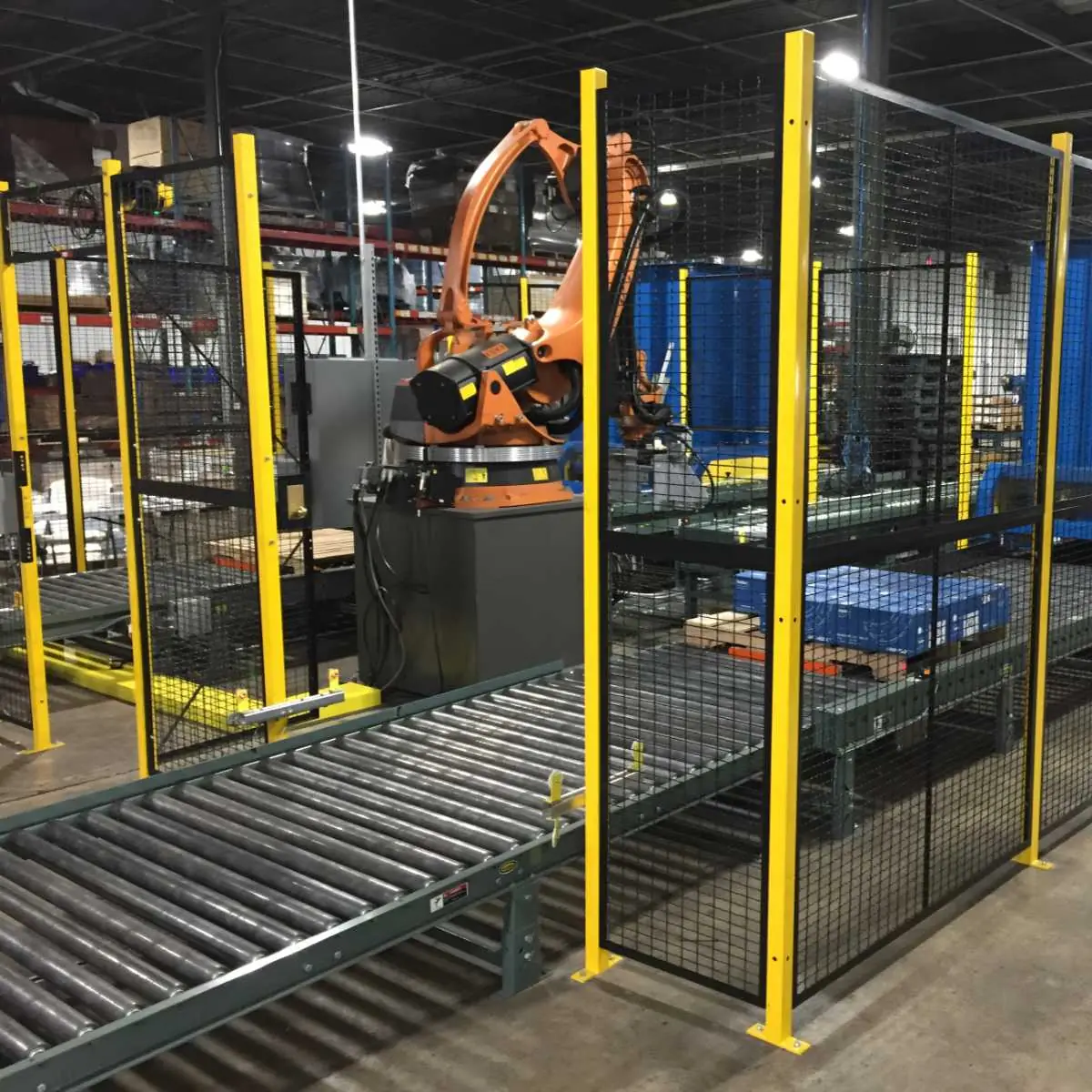 Black wire mesh machine guarding with yellow posts around a robotic conveyor cell