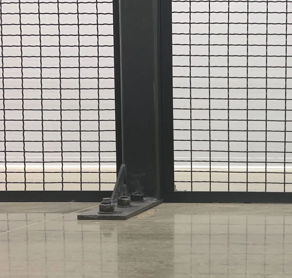 Wire mesh partition panel mounted flush to the floor beside an anchored post base plate